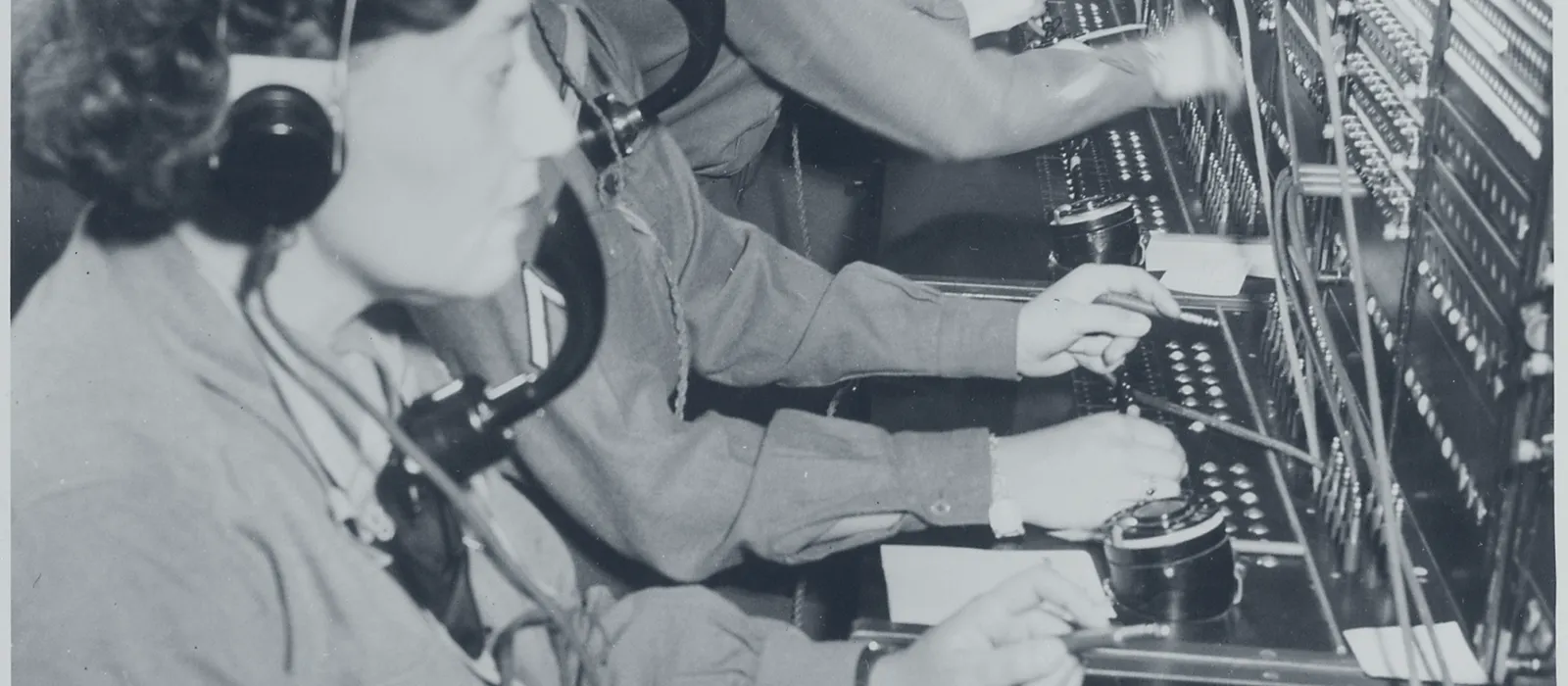 Rangée d'opératrices casque sur les oreilles devant un standard téléphonique manuel, chacune enfichant des fiches dans un mur de connecteurs.